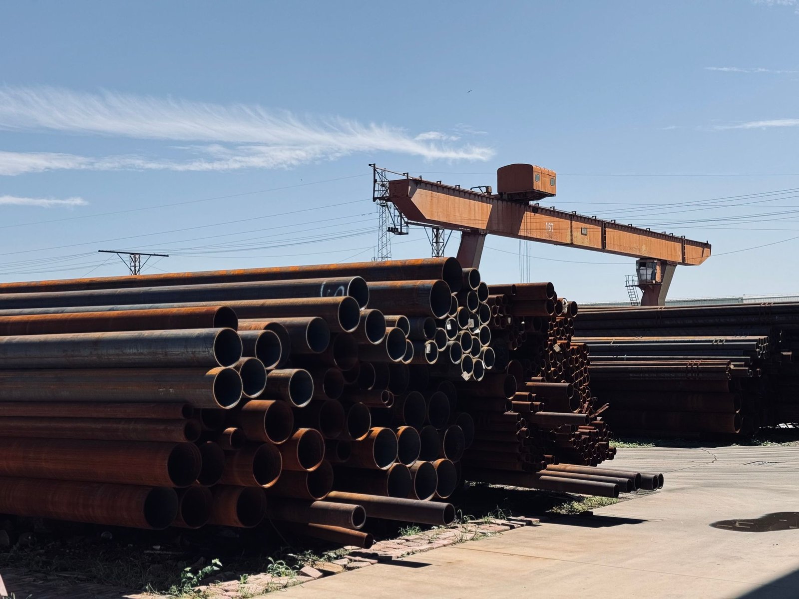 Steel tubulars racked in an industrial storage yard beneath an overhead crane.